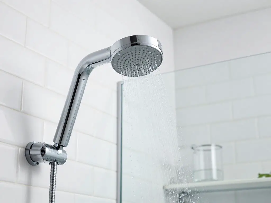 bathroom interior detail shot showing modern chrome low-flow showerhead with water droplets, clean white subway tiles, clear glass shower do.