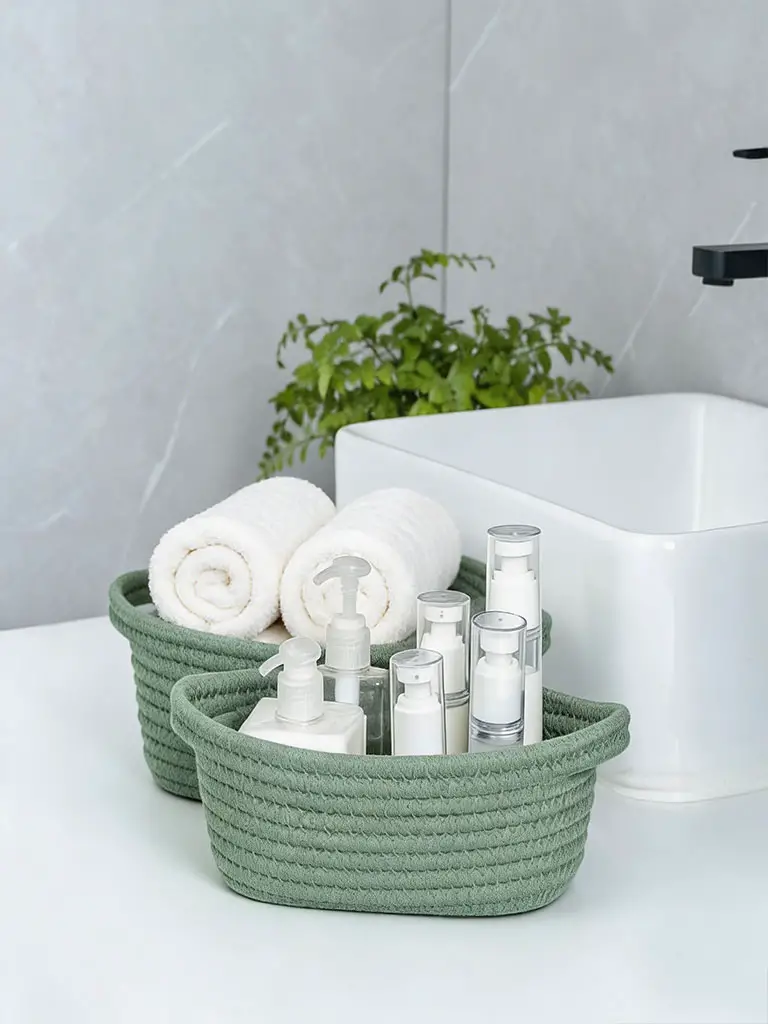 Olive green woven storage baskets on bathroom countertop with rolled white towels and skincare bottles.