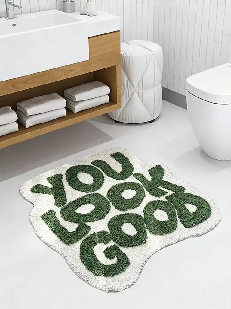 Olive green and cream you look good bath mat on white bathroom floor near wood vanity and toilet.