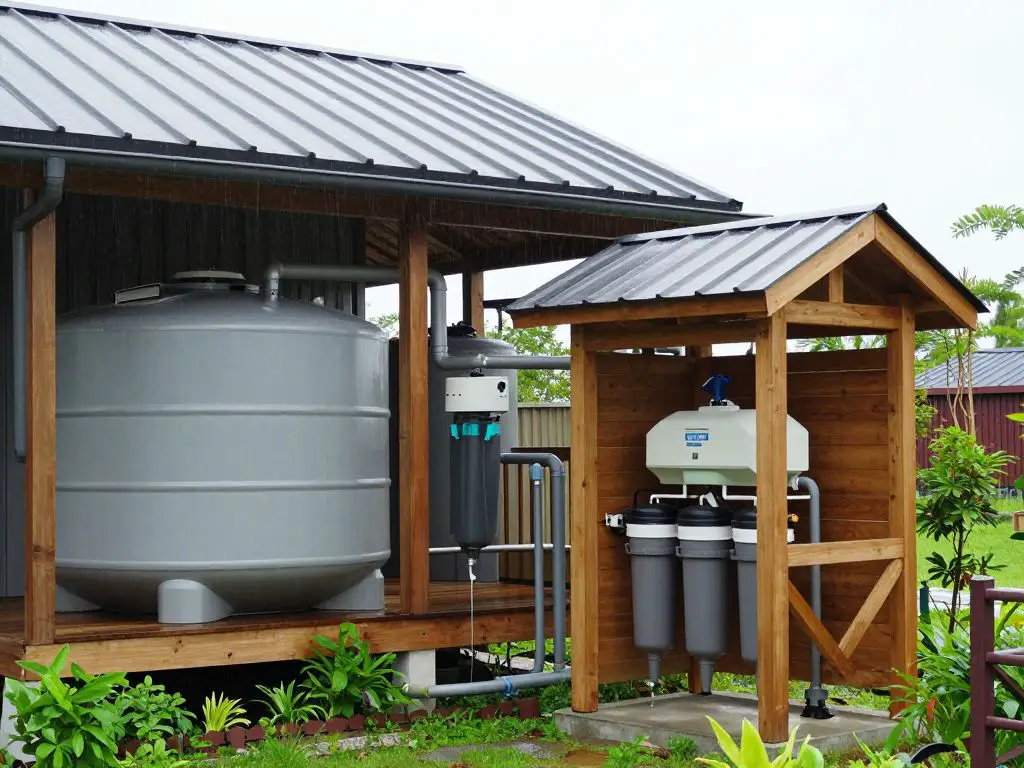 photograph of cabin rainwater collection system integrated into design, large storage tanks visible beneath deck, metal roof with clean gutt.