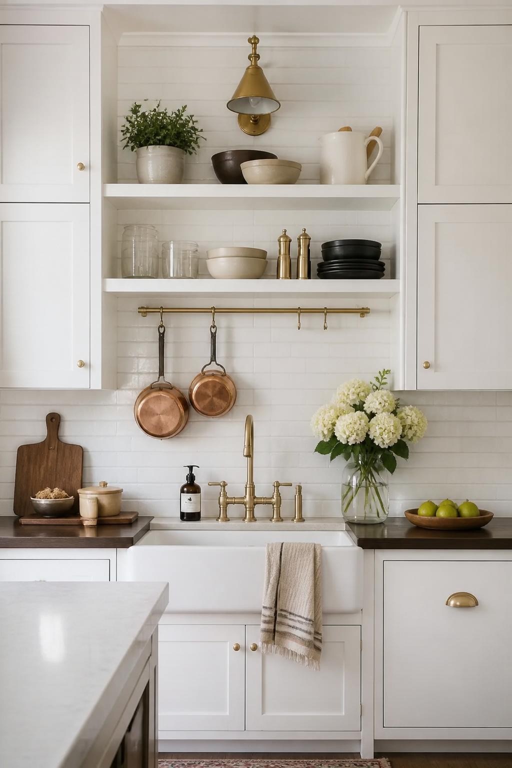 A timeless white kitchen styled with gold and brass accents features two bright white floating shelves mounted between tall cabinetry, illum.